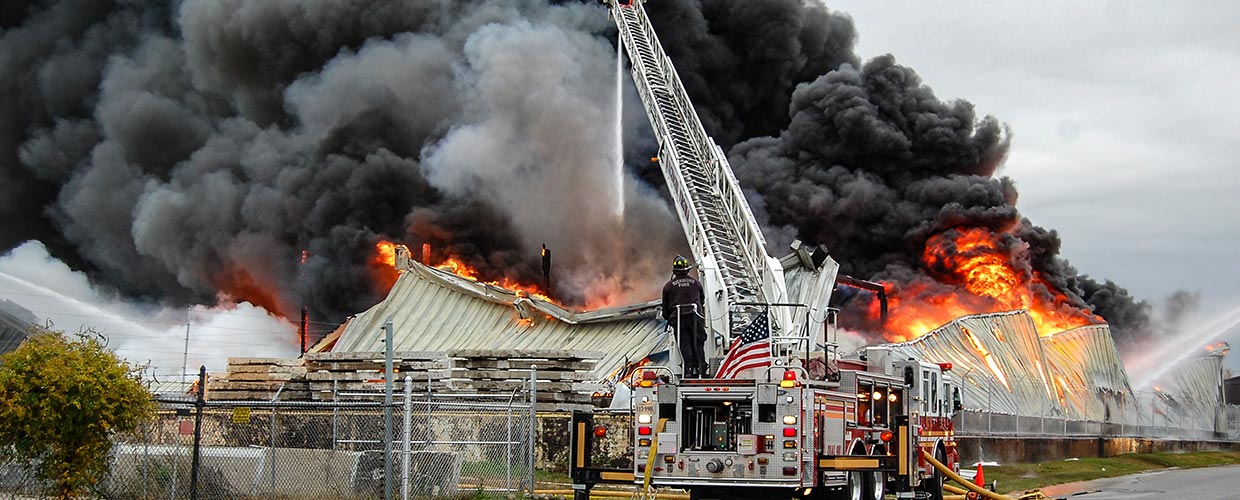 Firefighter on ladder truck hoses water onto a building fire.